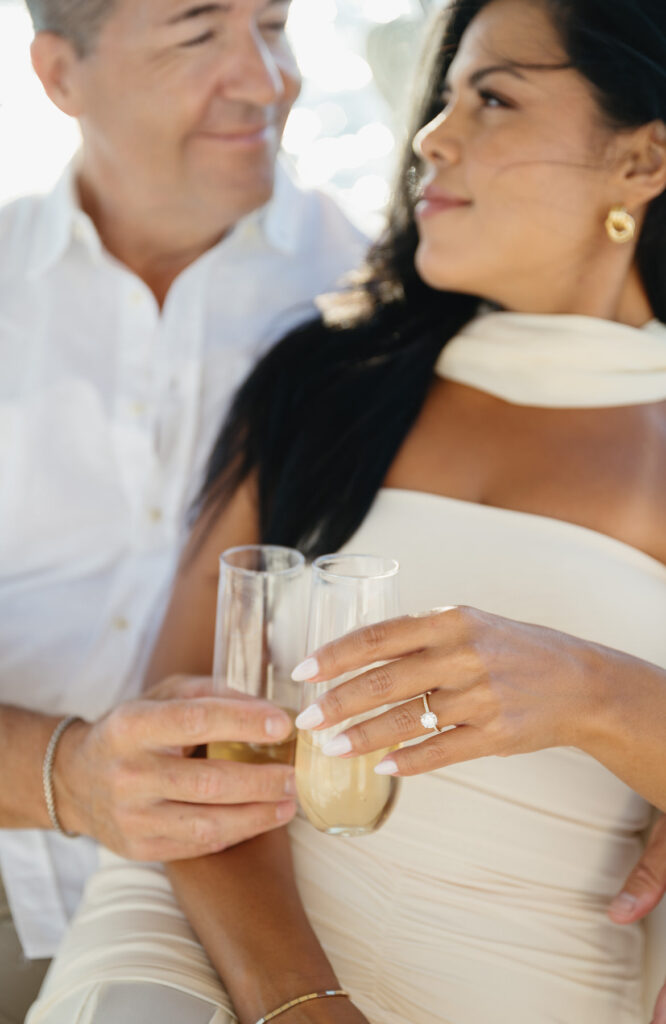 engaged couple clinks their champagne glasses together while sailing