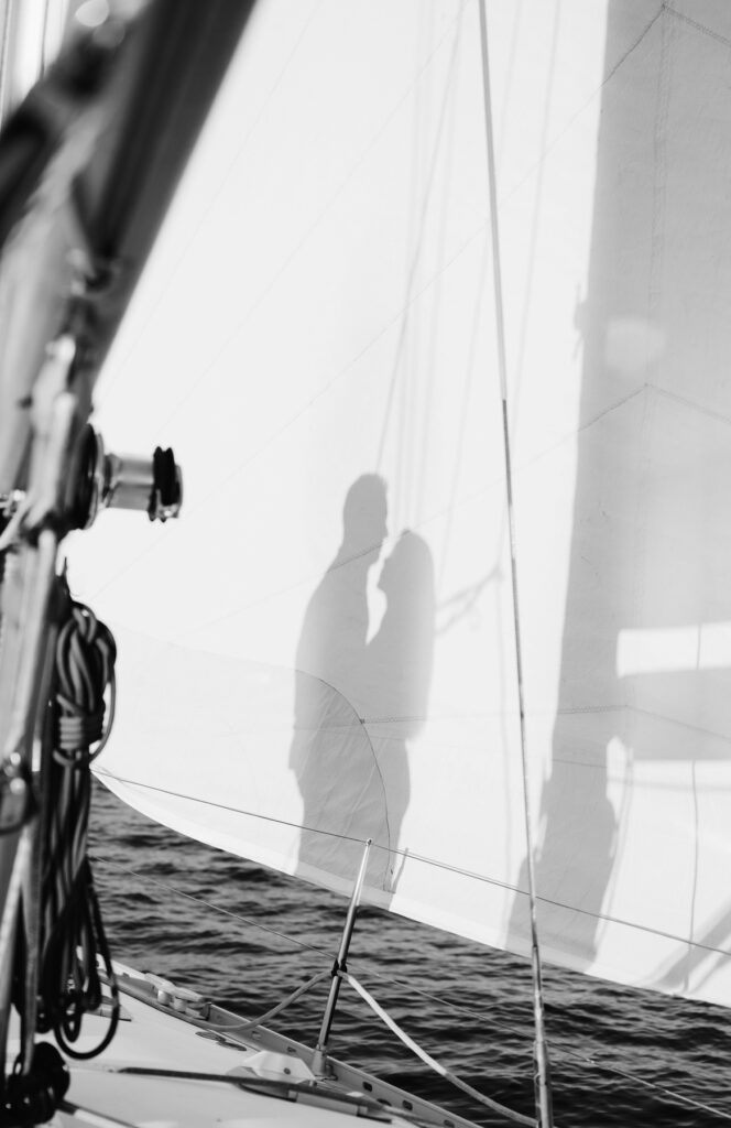 shadow of a woman chest to chest with her fiance on the sail of a sailboat at sunset