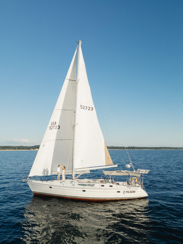 man twirls his fiance while sailing on a sailboat on Lake Michigan at sunset