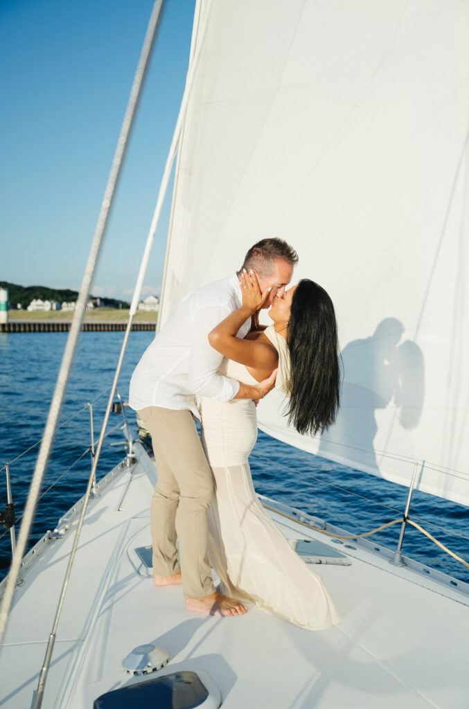 woman leans back and she kisses her fiance on a sailboat on Lake Michigan at sunset