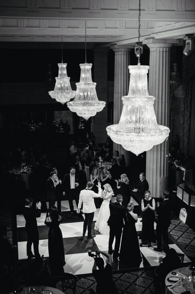 bride and groom dancing with their wedding guests on a black and white checkered dance floor under chandeliers at the Ballroom at McKay